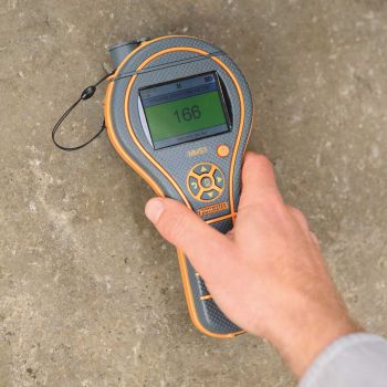 Abgebildet ist das Feuchtigkeitsmessgerät MMS-3 der Firma PROTIMETER. Das Gerät wird in einer Hand gehalten, während mit der anderen Hand eine Widerstandselektrode in eine Holzoberfläche gedrückt wird, um die Holzfeuchte zu messen.